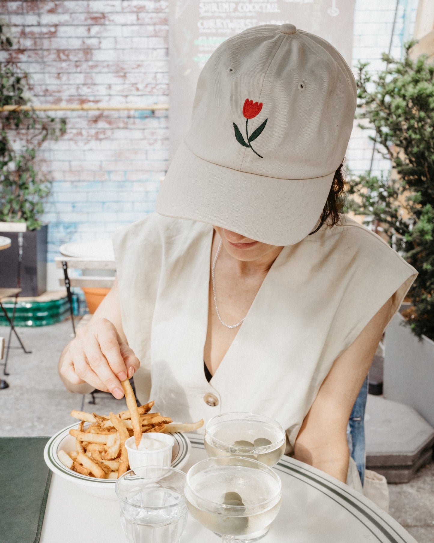 Person wearing a beige cap with a tulip design, sitting at a table with food and drinks.