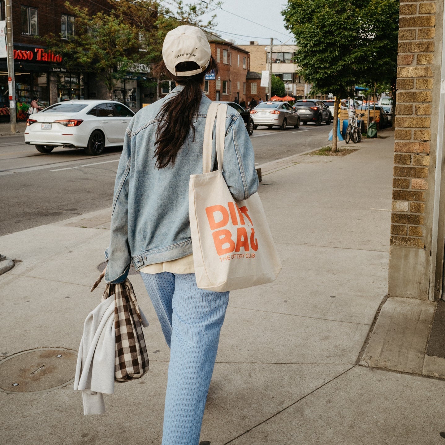 Person walking on sidewalk holding a tote that says Dirt Bag.