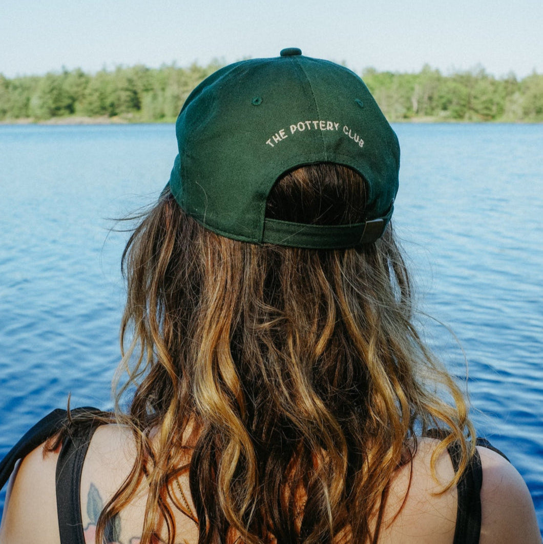 Person with tattoos wearing a green cap sitting by a lake