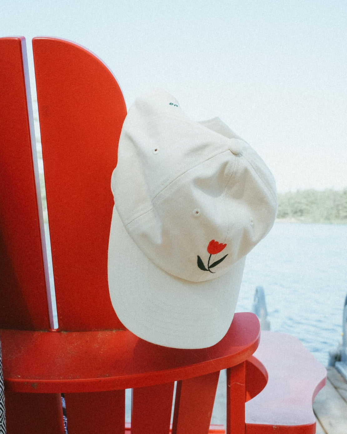 White cap with a red flower design on a red chair by a body of water.