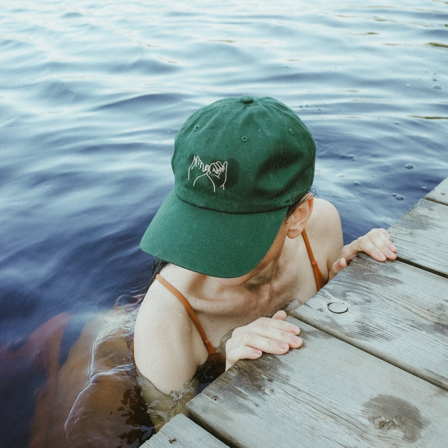 Person wearing a green cap and swimsuit, partially submerged in water on a wooden dock.