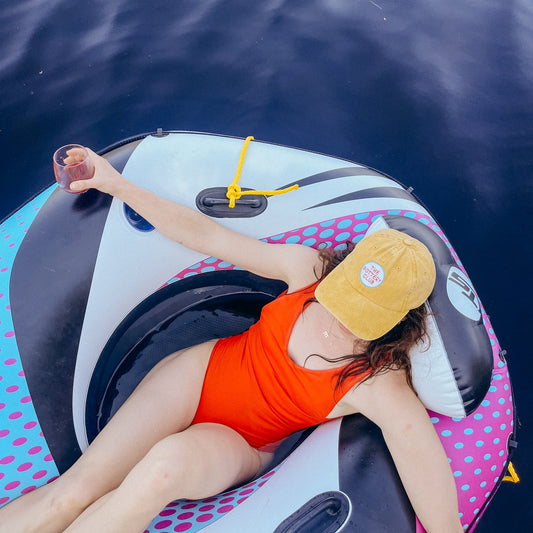 Person lying on an inflatable tube in the water wearing a yellow cap and orange swimsuit.