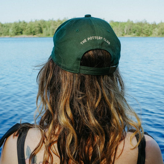 Person with tattoos wearing a green cap sitting by a lake
